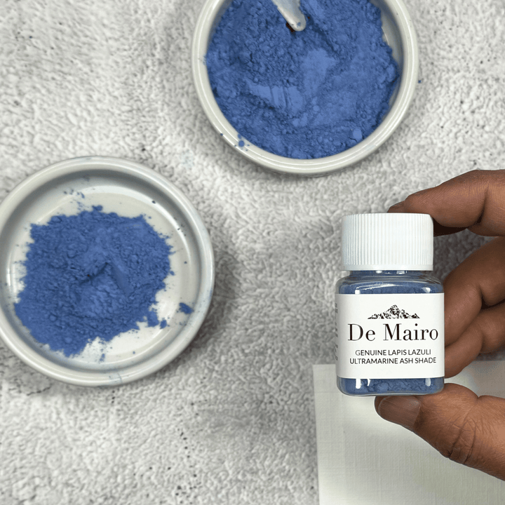 Genuine Lapis Lazuli Ultramarine Ash Shade Pigment jar holding in fingers over dishes of dry pigment