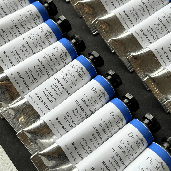Multiple tubes of De Marte gouache paint on a dark surface