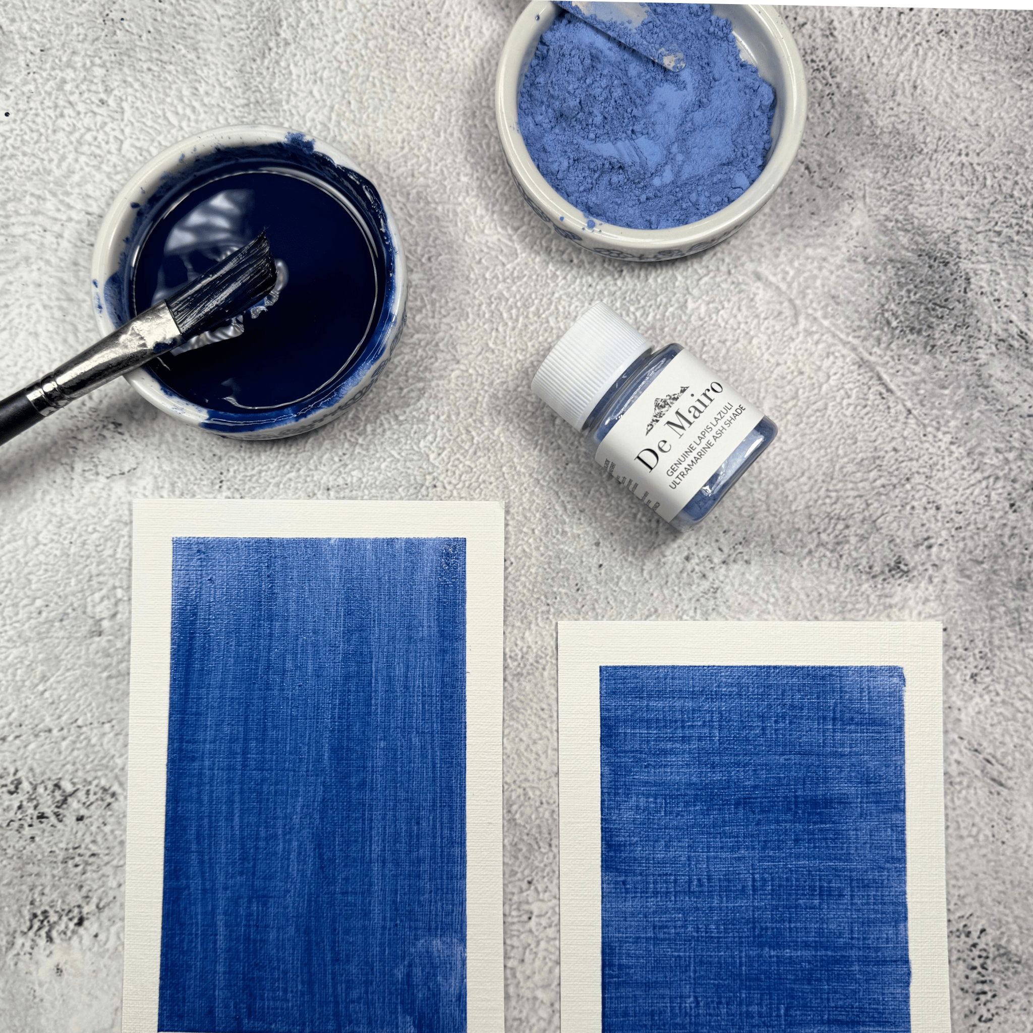 Ultramarine Ash Shade oil medium swatches near a pigment jar, a dish with powdered pigment and another dish with blended pigment with paint brush in it 