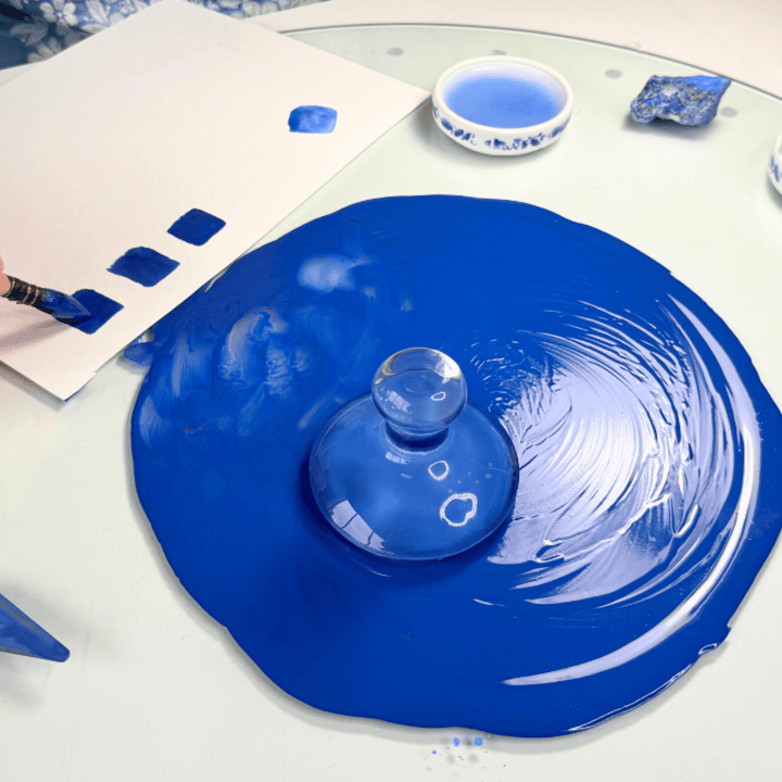 Blue glass lid on a white surface with a brush and blue paint.