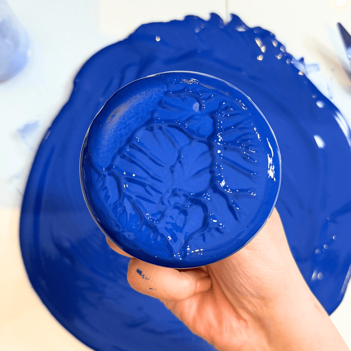 Hand holding a blue glass plate with lapis lazuli gouache against a white background