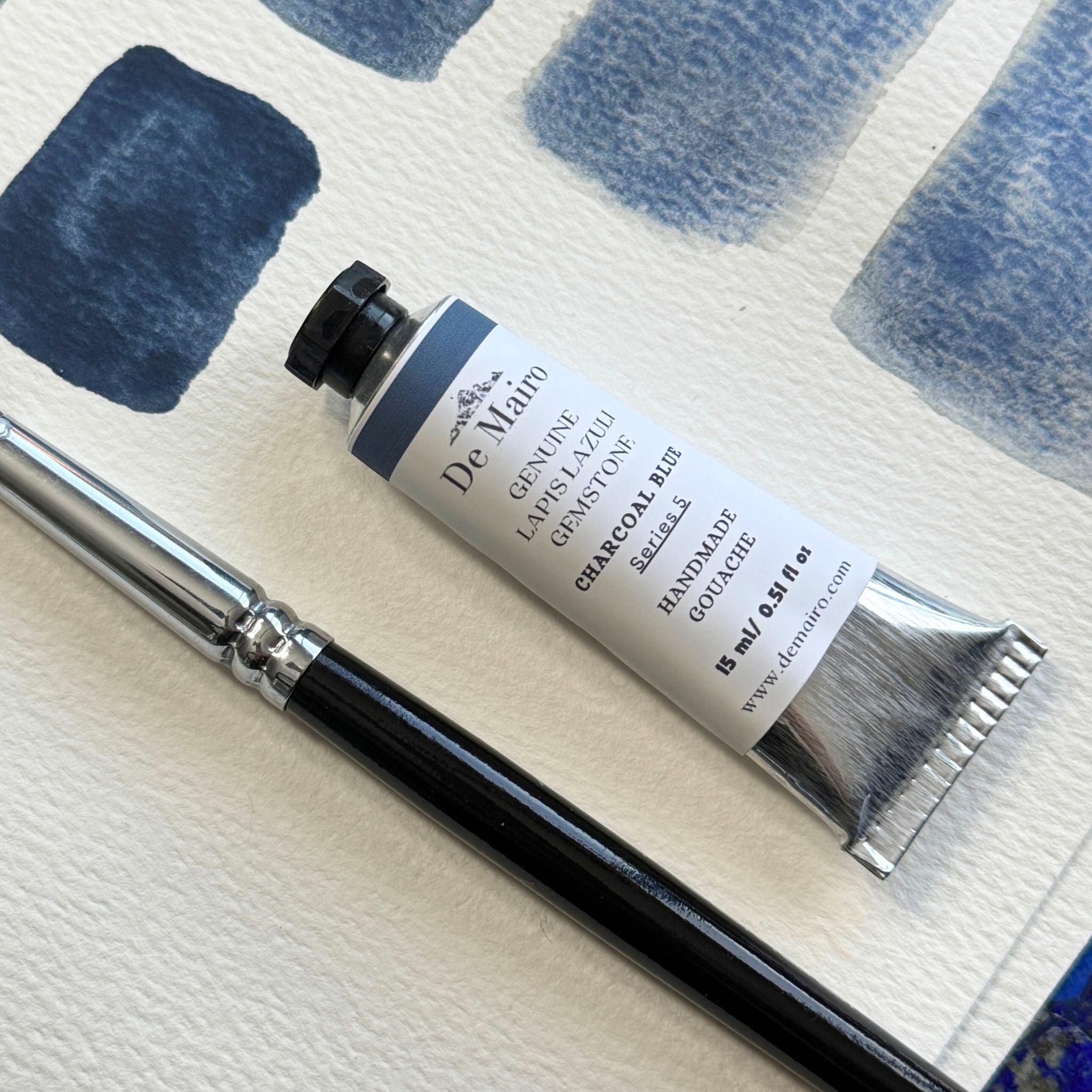 Tube of De Mairo charcoal blue gouache with a brush on a textured surface